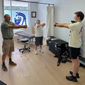An older man and woman doing a body and balance stretch with a physio