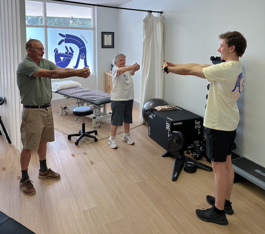 An older man and woman doing a body and balance stretch with a physio